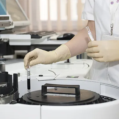 Gloved hands placing a blood tube into an analyzer