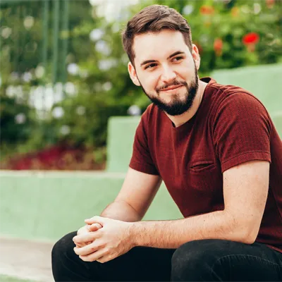Young man sitting relaxed on steps in a green outdoor setting